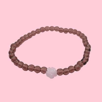 An elastic beaded bracelet composed of light burgundy 4mm glass beads, featuring a single translucent pink flower bead at the centre, shown on a white background.