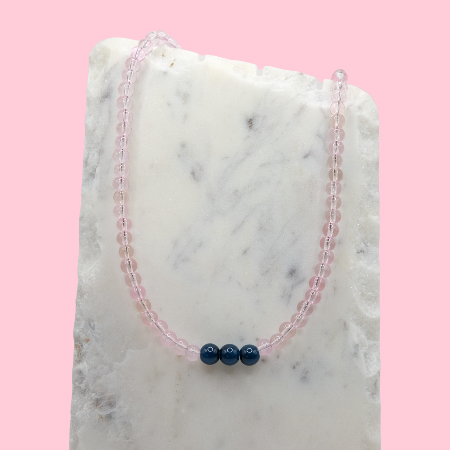Beaded necklace with pink and blue beads on a marble surface with a pink background