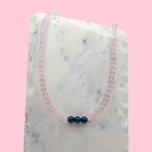 Beaded necklace with pink and blue beads on a marble surface with a pink background