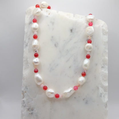 A beaded necklace composed of pink opal beads, red agate beads and freshwater pearl nuggets - arranged in an alternating pattern, shown on a white marble background.