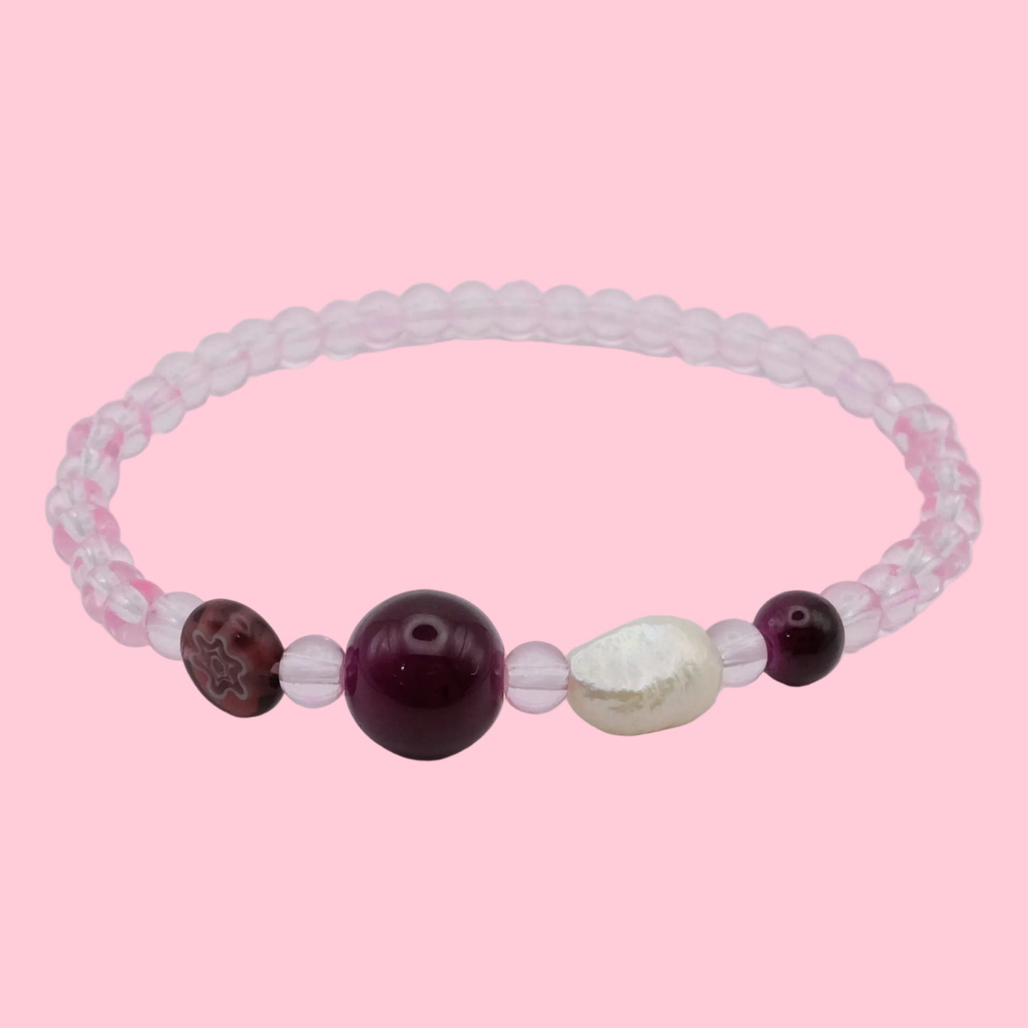 An elastic beaded bracelet composed of translucent pink 4mm glass beads, featuring burgundy glass feature beads, a marbled burgundy accent bead, and a freshwater pearl, shown on a white background.