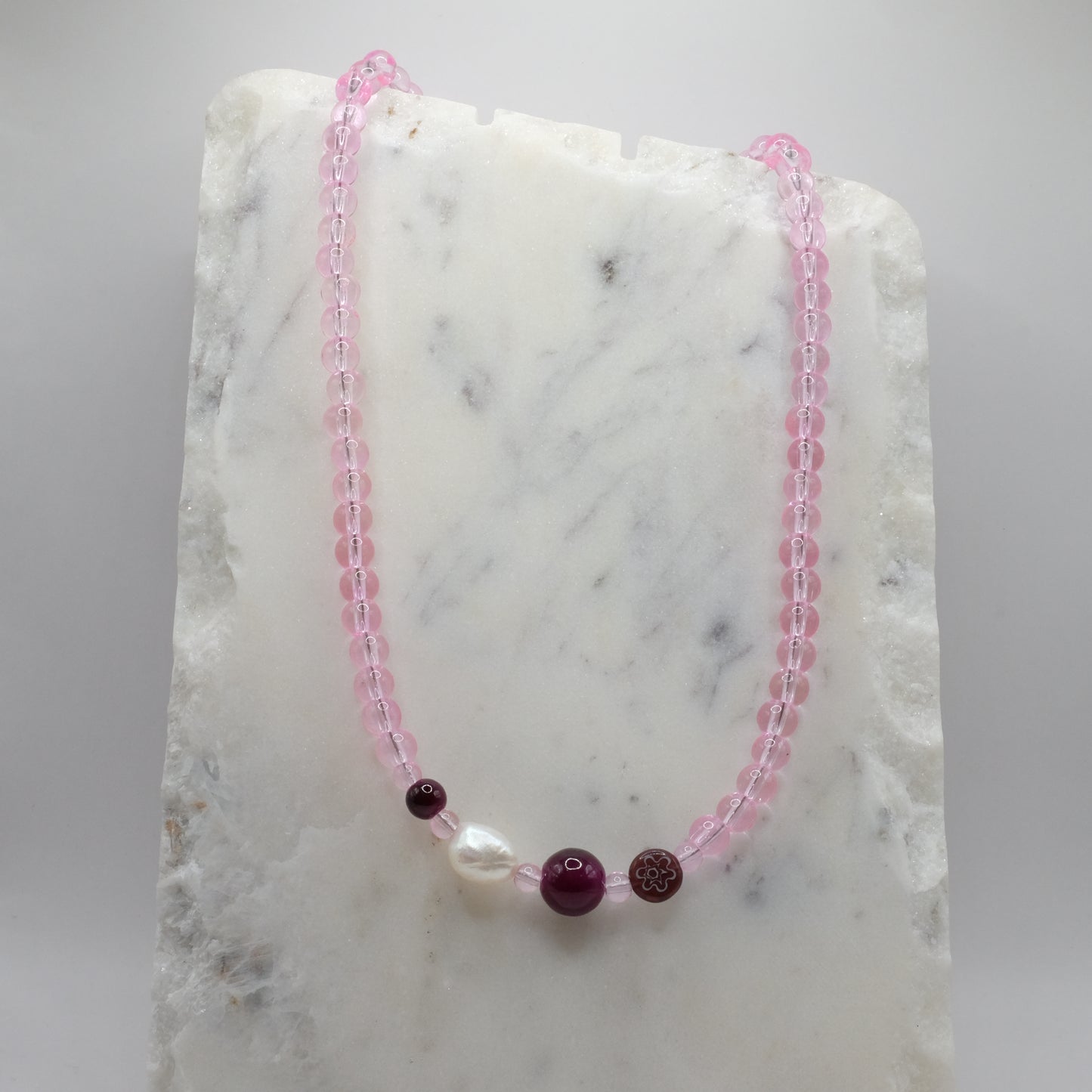 Beaded necklace with pink and purple beads on a marble surface