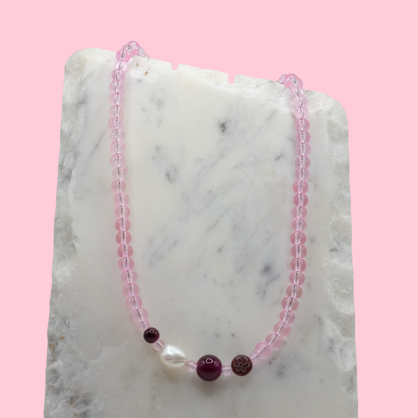 Necklace with pink beads and a central pearl on a marble surface with a pink background