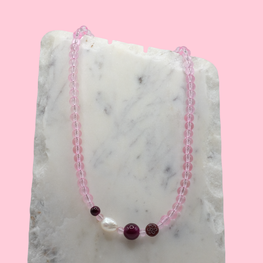 Necklace with pink beads and a central pearl on a marble surface with a pink background