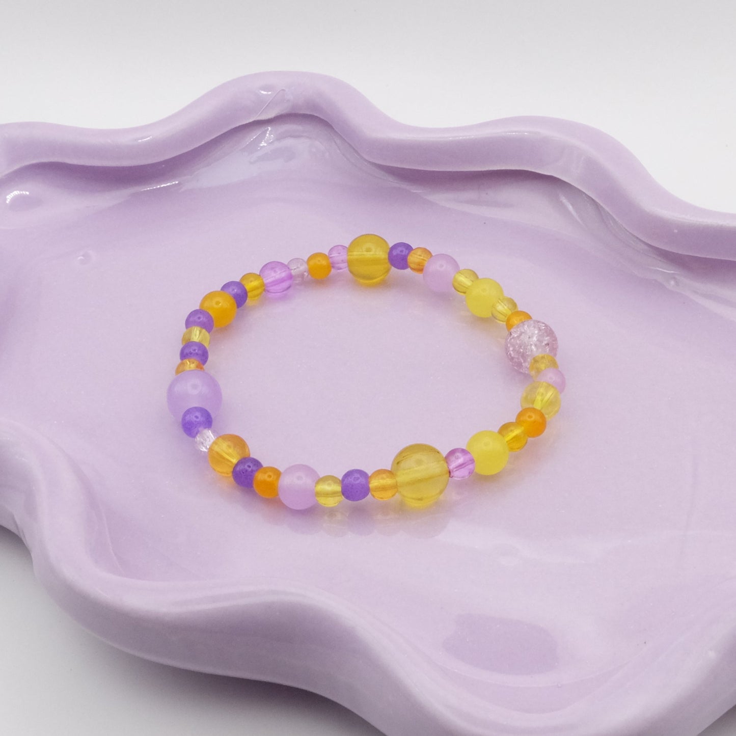 An elastic beaded bracelet made of 4mm, 6mm, and 8mm glass beads in various shades of light and dark purple and sunny yellows, displayed on a simple surface.