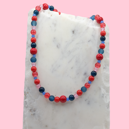 Beaded necklace with red, blue, and pink beads on a marble surface with a pink background
