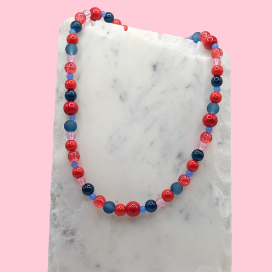 Beaded necklace with red, blue, and pink beads on a marble surface with a pink background