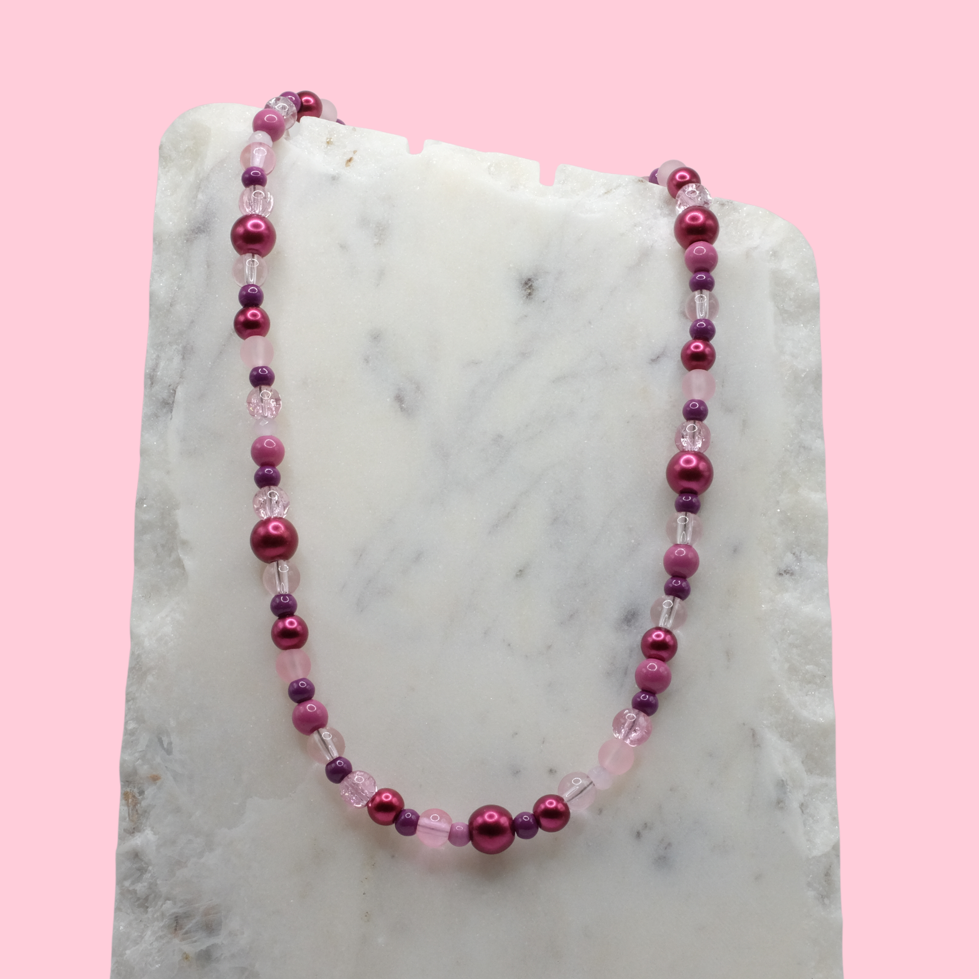 Necklace with pink and purple beads on a marble surface with a pink background