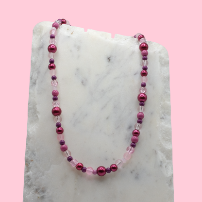 Necklace with pink and purple beads on a marble surface with a pink background