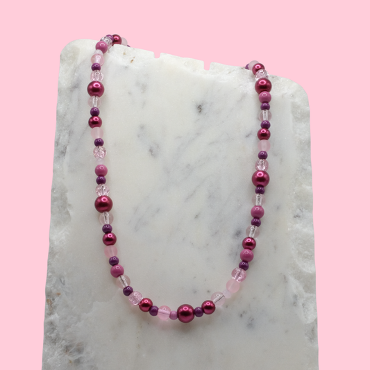 Necklace with pink and purple beads on a marble surface with a pink background