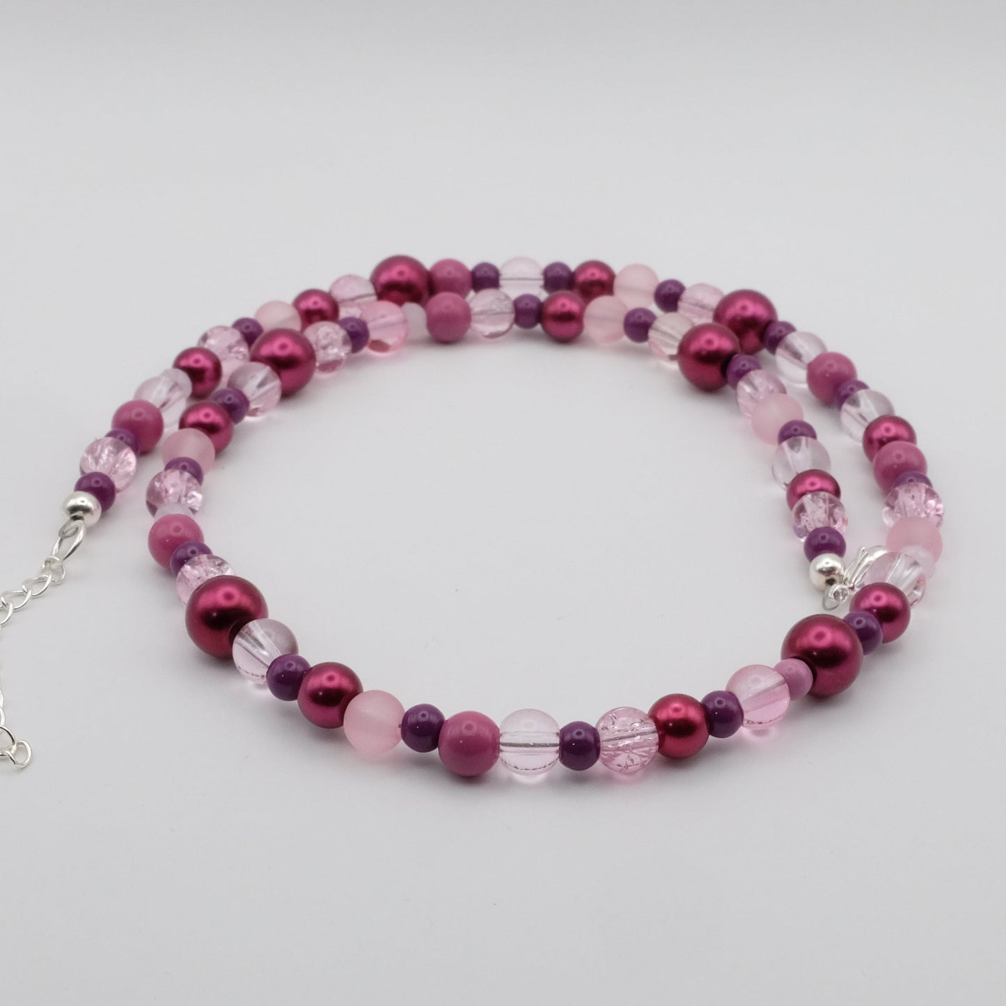 A handmade beaded necklace featuring a mix of 4mm, 6mm, 8mm and 10mm glass beads in pink, plum and soft purple tones, displayed on a white background.