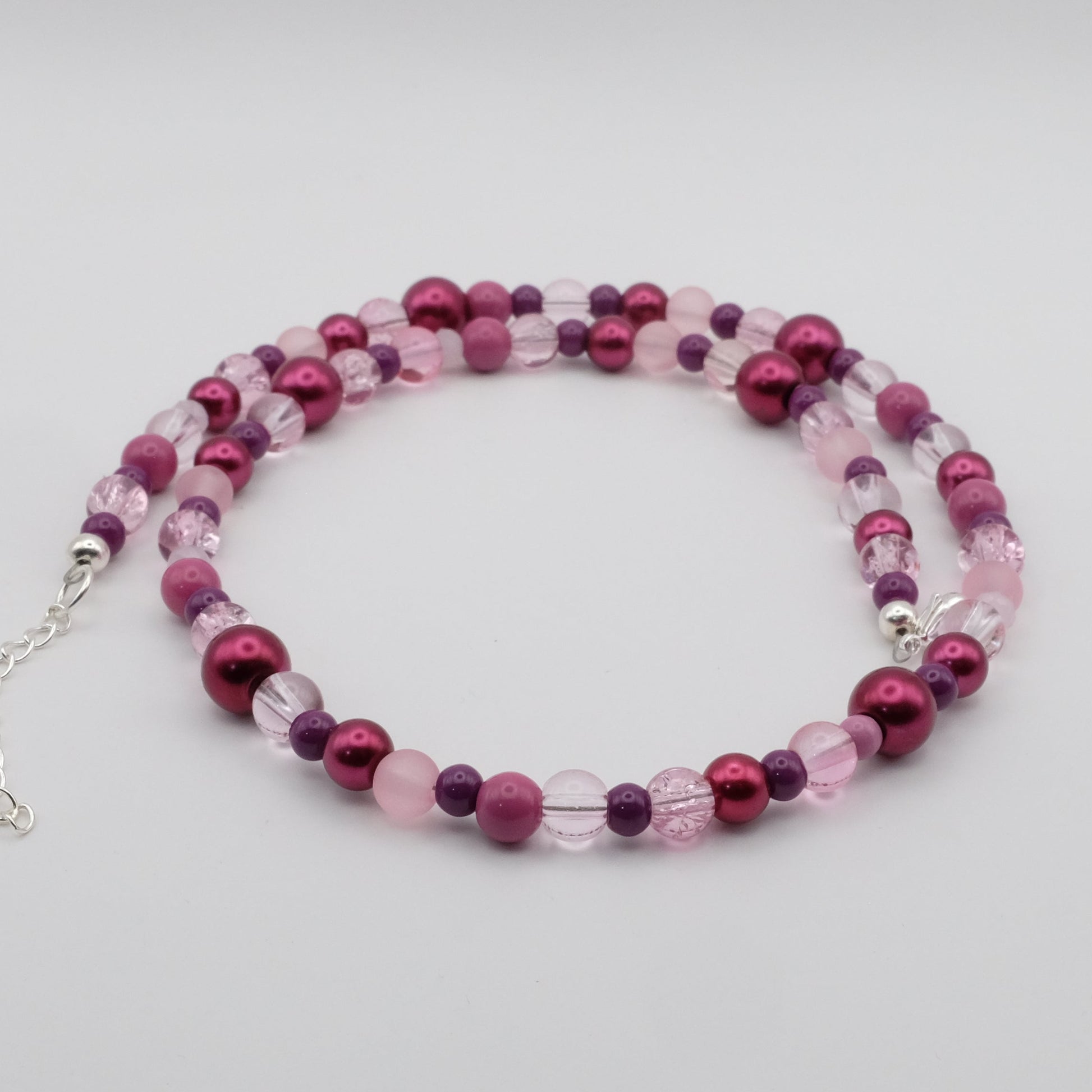A handmade beaded necklace featuring a mix of 4mm, 6mm, 8mm and 10mm glass beads in pink, plum and soft purple tones, displayed on a white background.