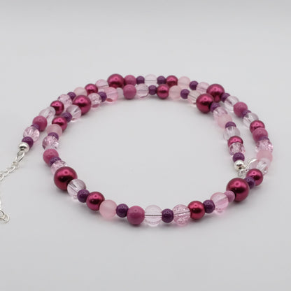 A handmade beaded necklace featuring a mix of 4mm, 6mm, 8mm and 10mm glass beads in pink, plum and soft purple tones, displayed on a white background.