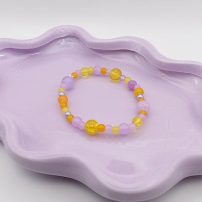 An elastic beaded bracelet made of 4mm, 6mm, and 8mm glass beads in shades of light purple and bright yellows, displayed on a simple surface.