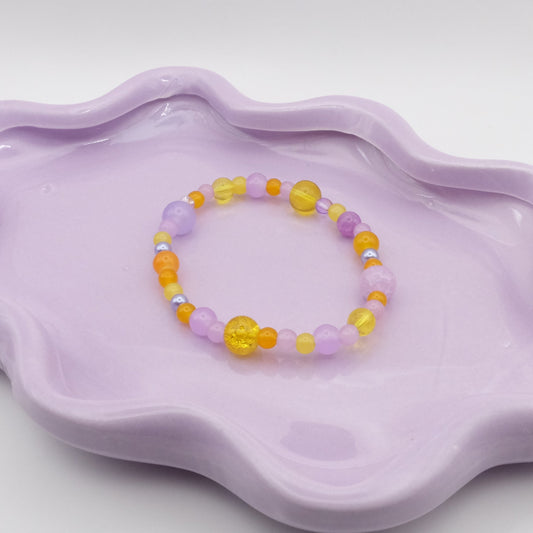 An elastic beaded bracelet made of 4mm, 6mm, and 8mm glass beads in shades of light purple and bright yellows, displayed on a simple surface.