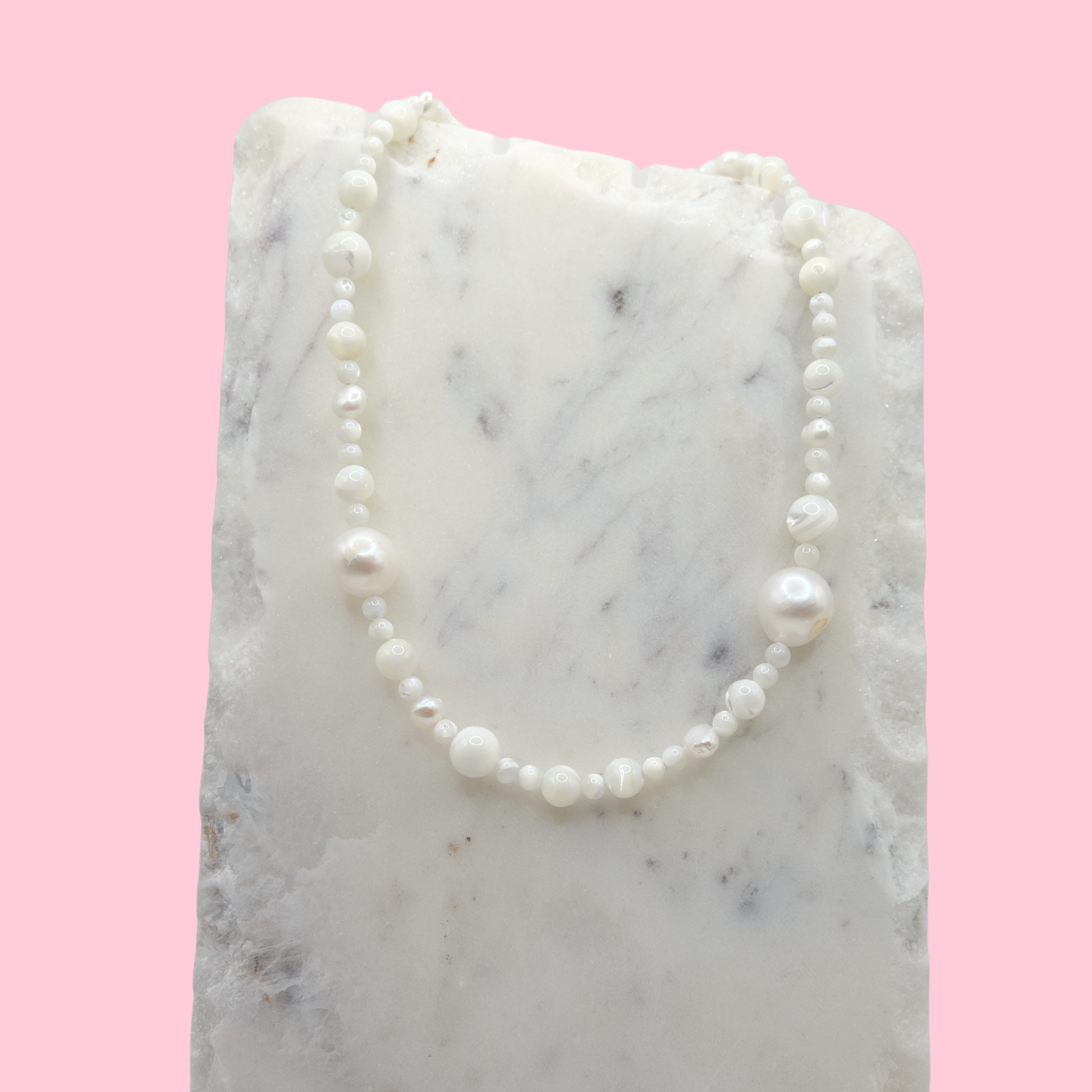 Pearl necklace on a marble surface with a pink background