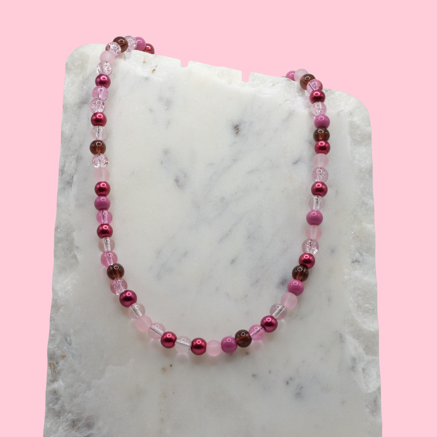 Beaded necklace with pink and brown beads on a marble surface with a pink background