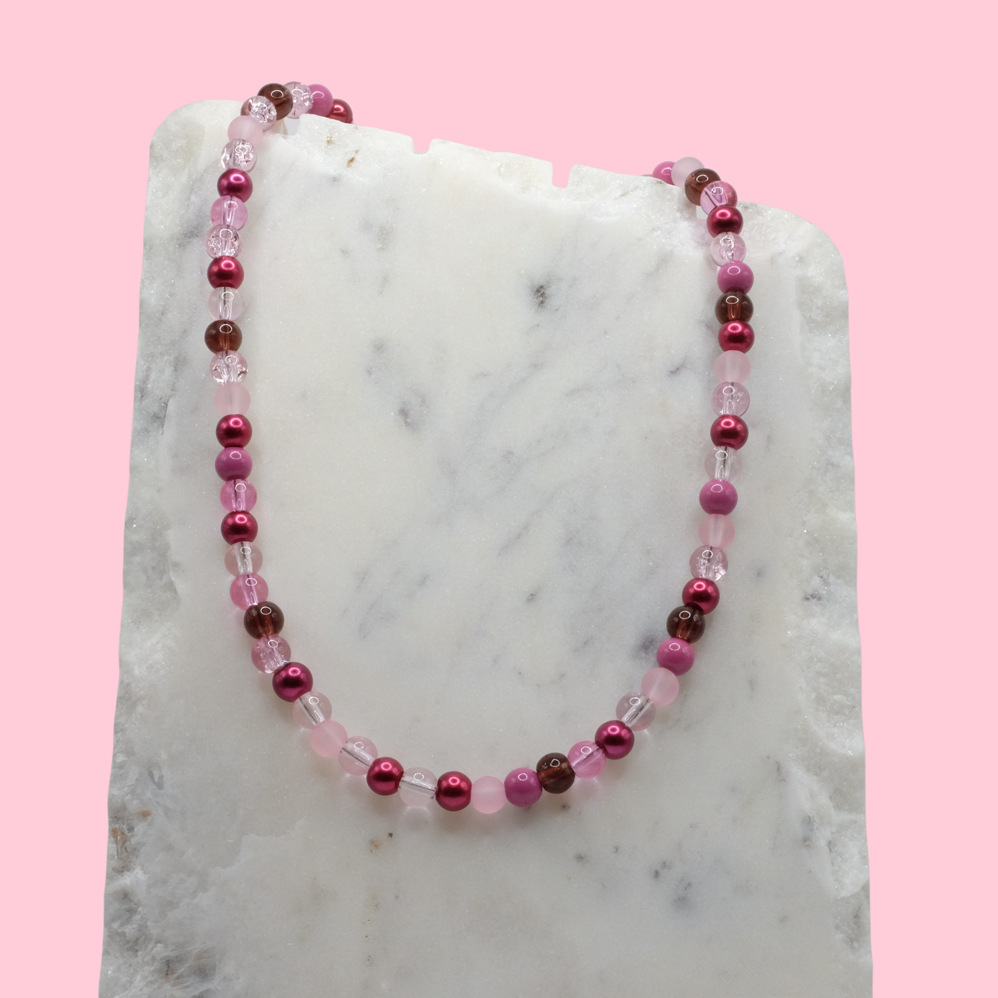 Beaded necklace with pink and brown beads on a marble surface with a pink background