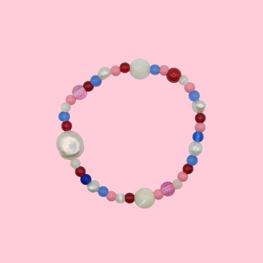 An elastic beaded bracelet composed of 4mm and 6mm glass beads in pink, red and blue - featuring mother of pearl and freshwater pearls, shown on a neutral background.