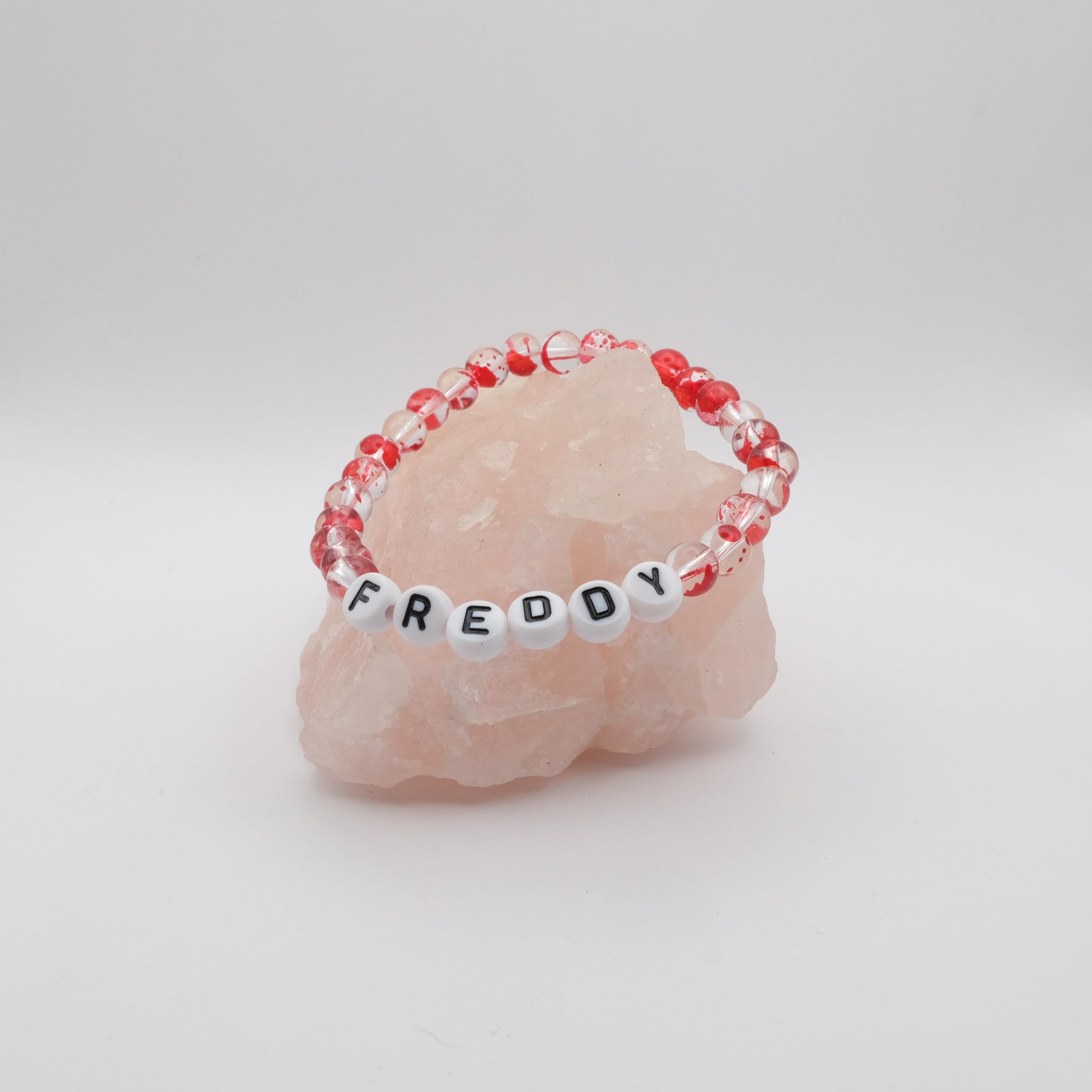 Bracelet with red and clear beads and letter beads spelling 'FREDDY' on a pink stone.