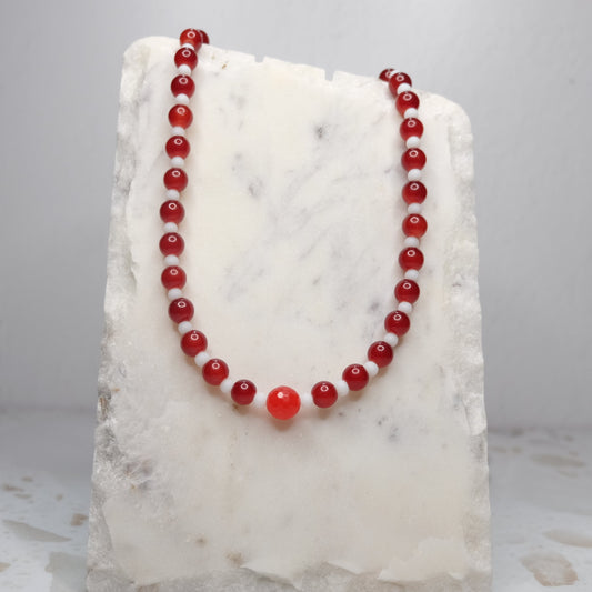 Red beaded necklace on a white marble block with a gray background