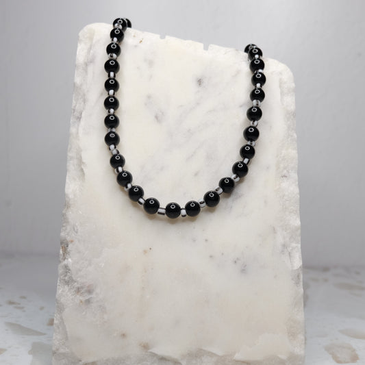 Black beaded necklace on a white marble stand against a light gray background