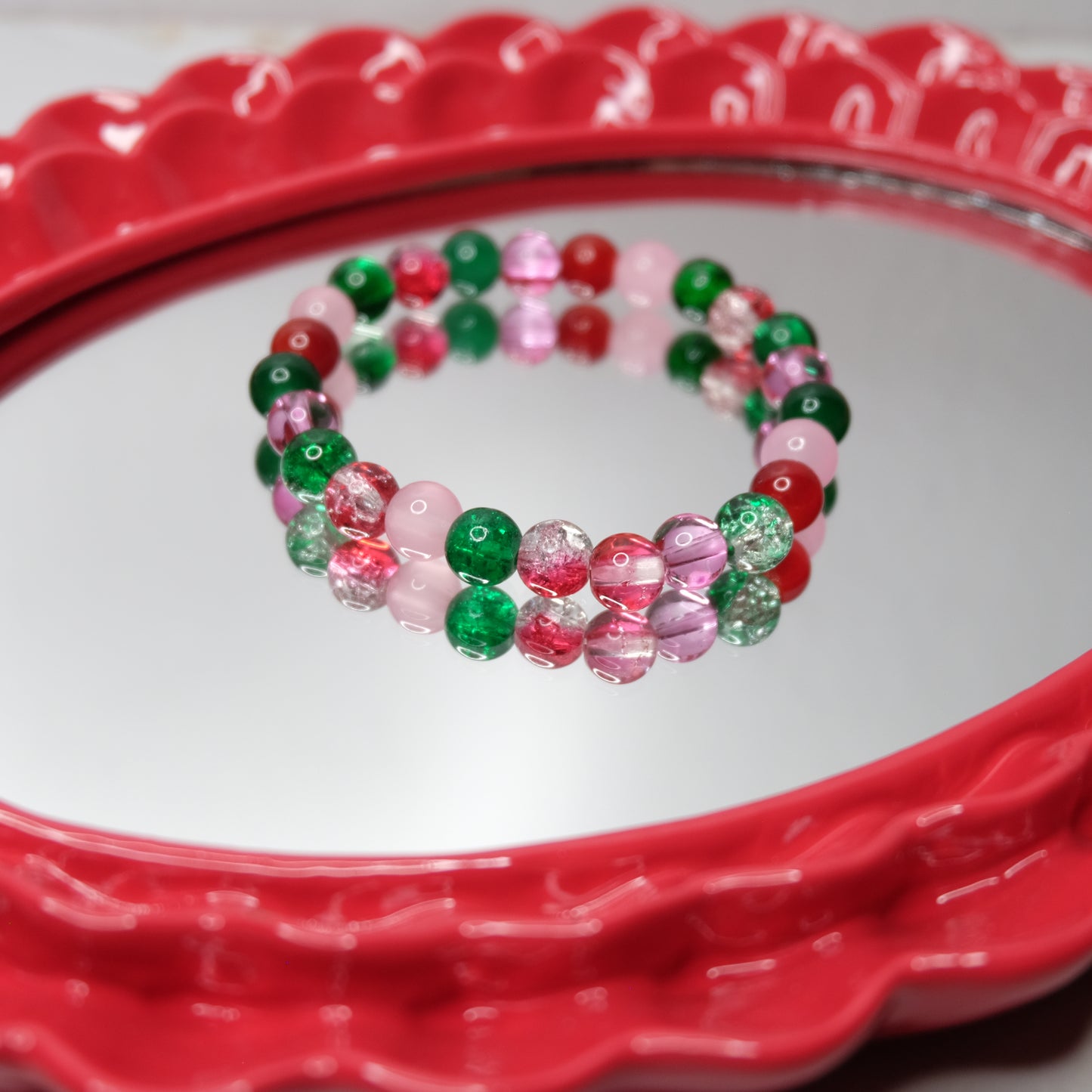 Pink, red and green elastic beaded bracelets on a red heart-shaped mirror