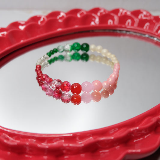 An elastic beaded bracelet in pink, red, green, clear and creams on a red textured surface