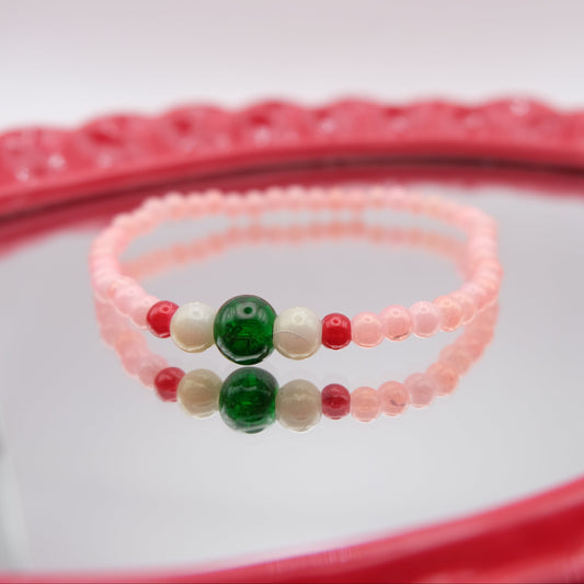 Beaded bracelet with green, red, and white beads on a pink background