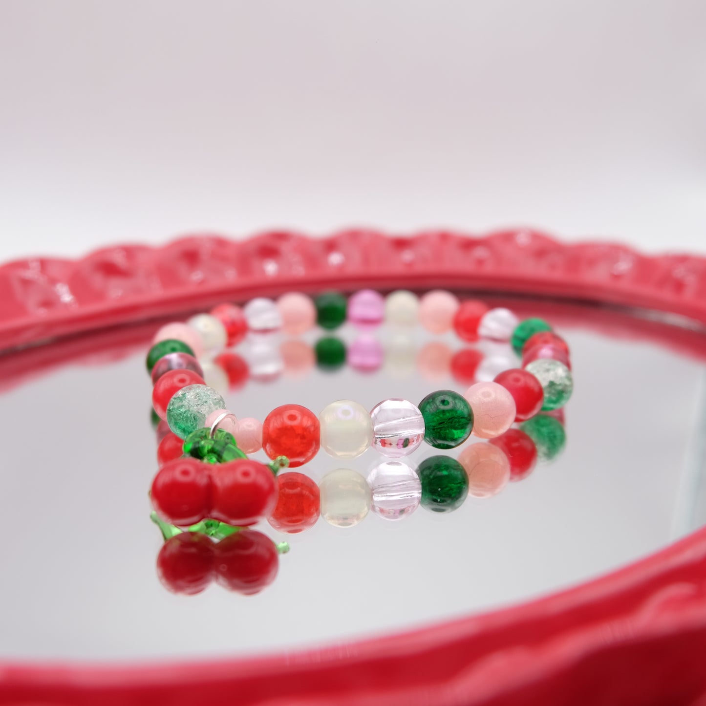 Beaded bracelet with red, green, and pink beads on a decorative red plate.
