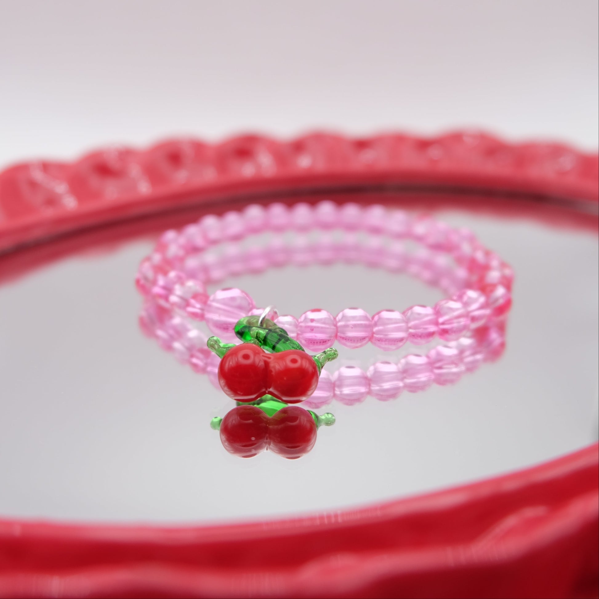 Pink beaded bracelet with cherry charm on a red and white background
