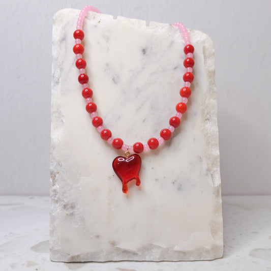 Red beaded necklace with a heart pendant on a marble stand.