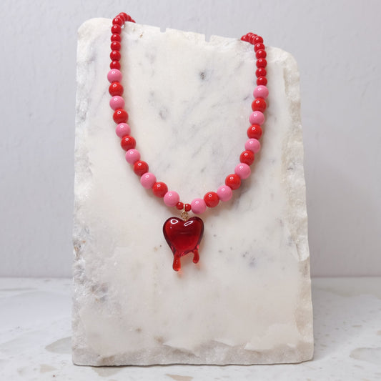 Necklace with red and pink beads and a heart pendant on a marble stand.