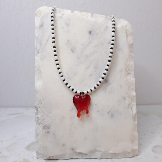 Necklace made from black and white seed beads with a red heart pendant on a marble stand