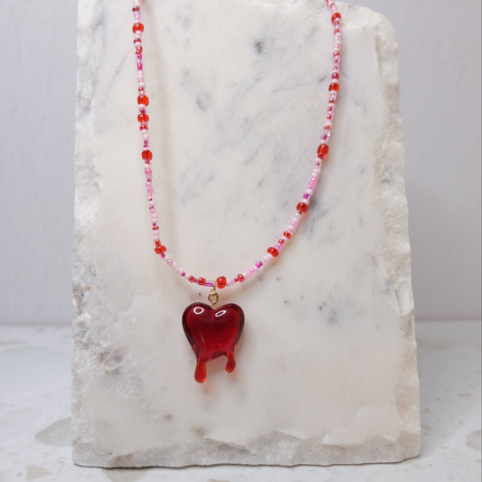 Pink and red necklace with a red heart pendant on a marble stand