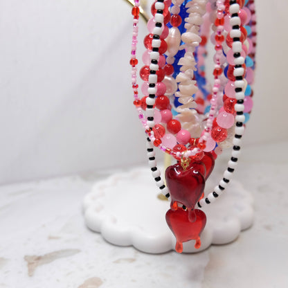 Beaded necklaces with heart pendants on a white stand
