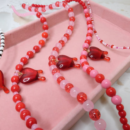 Necklace with red and pink heart-shaped beads on a pink surface