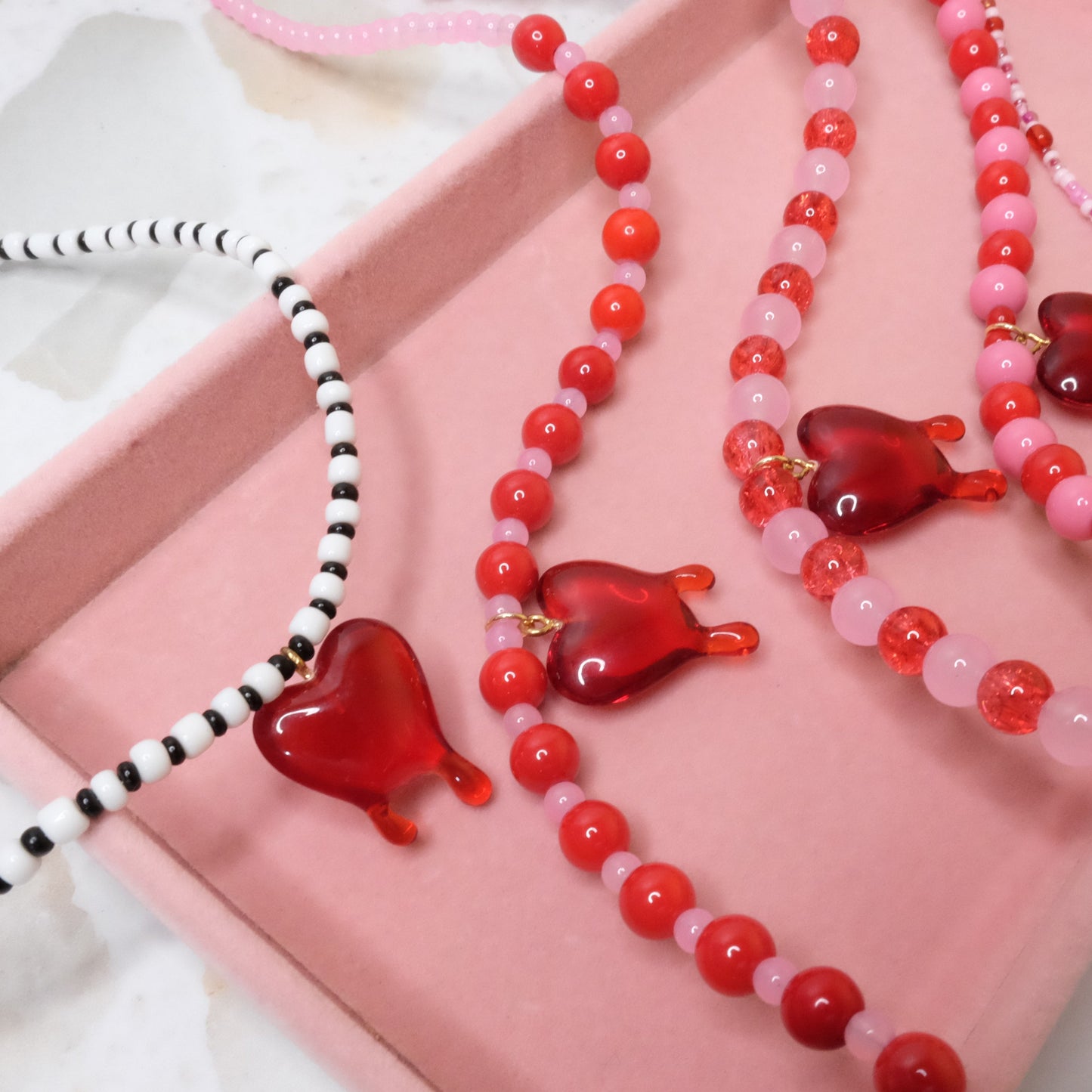Necklaces with red heart-shaped beads and pink and white accents on a pink surface.