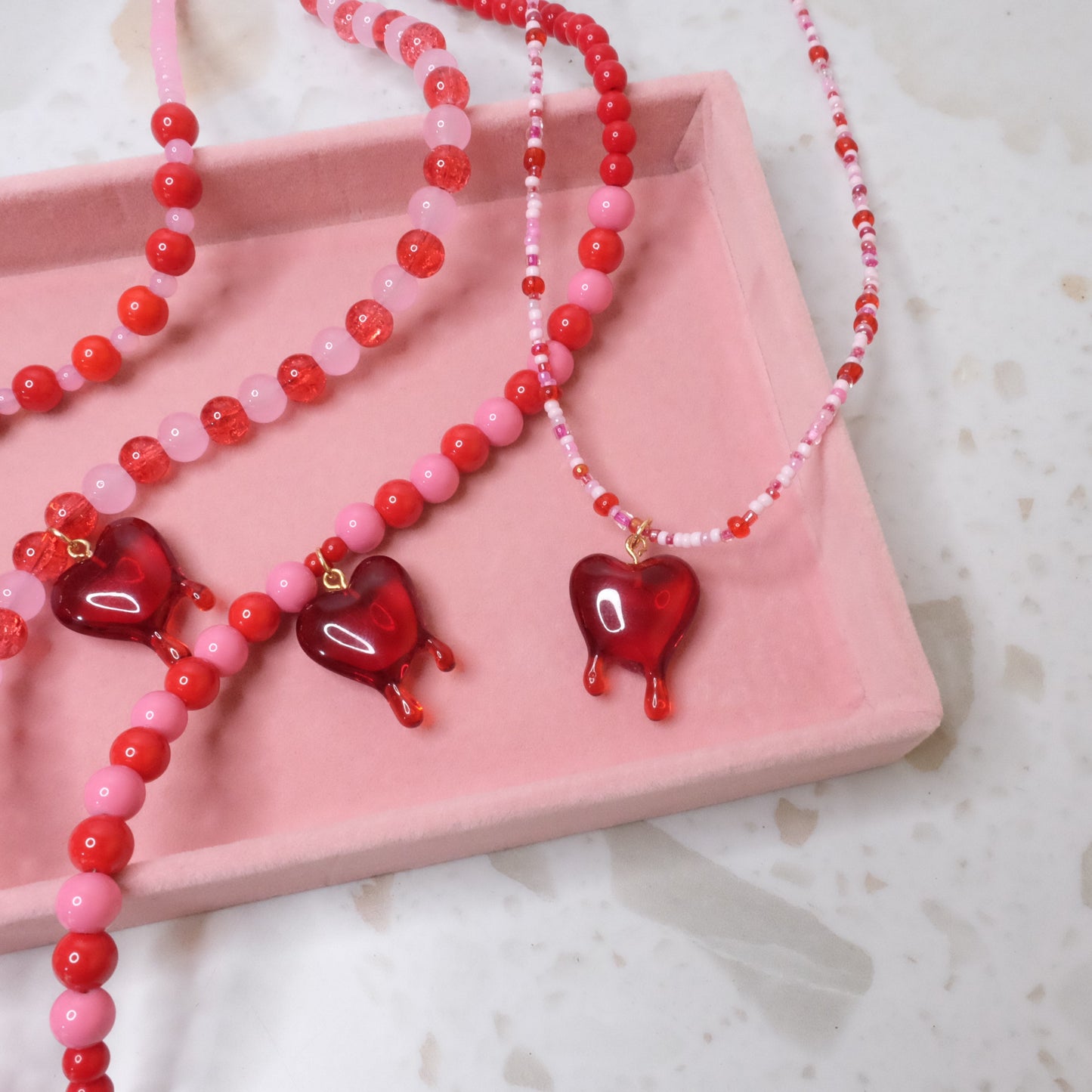 Pink and red necklace with red heart pendants on a pink tray