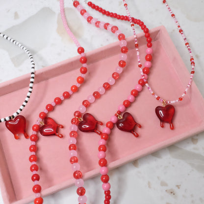 Multiple beaded necklaces with heart charms on a pink tray.
