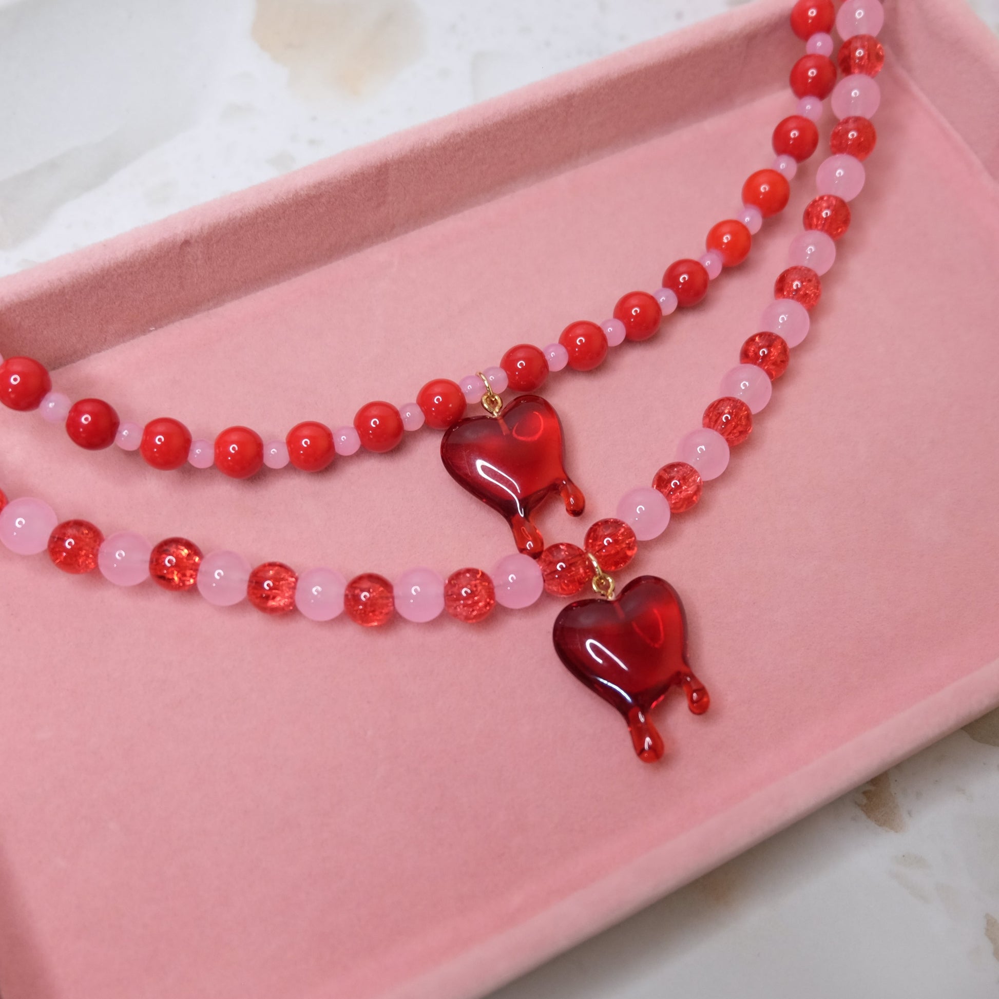 Beaded necklace with red heart pendants on a pink tray