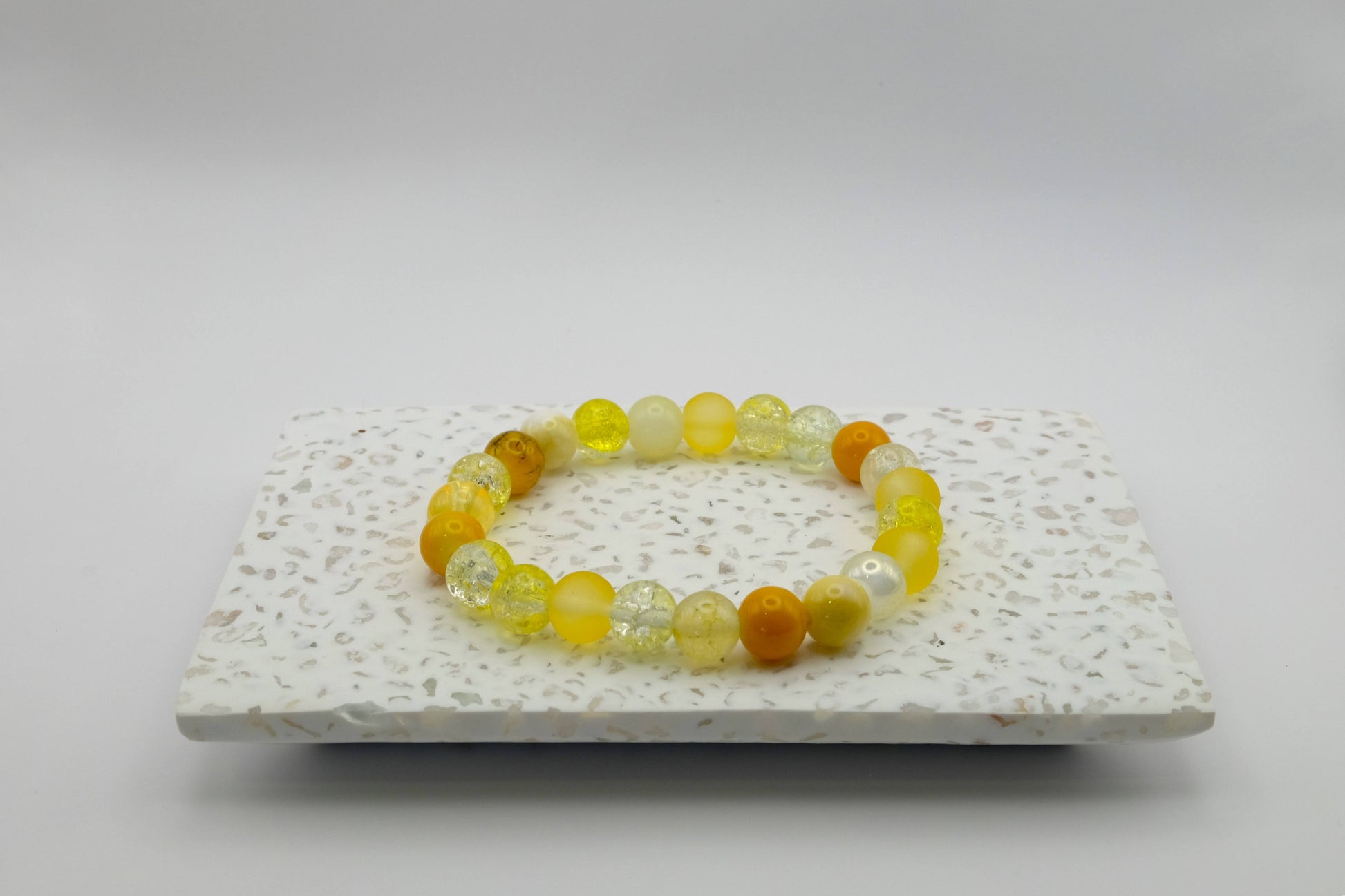 An elastic beaded bracelet composed of 8mm yellow glass beads featuring frosted, crackle, and pearl-like textures, shown on a terrazzo tile.