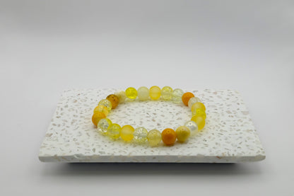 An elastic beaded bracelet composed of 8mm yellow glass beads featuring frosted, crackle, and pearl-like textures, shown on a terrazzo tile.