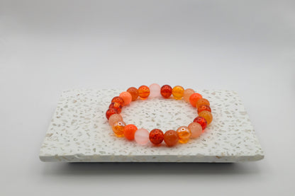 An elastic beaded bracelet composed of 8mm orange toned glass beads featuring frosted and crackle finishes, shown on a terrazzo tile surface.