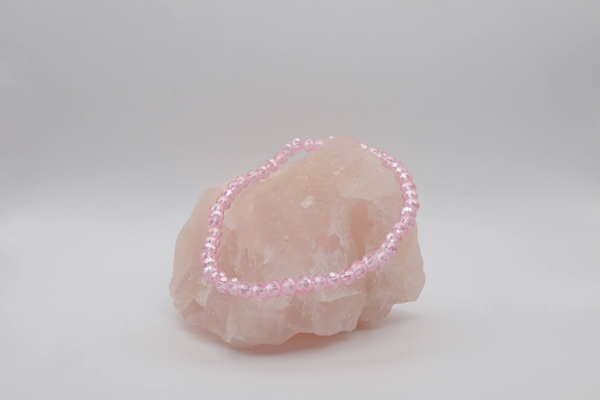 A pink beaded bracelet made with faceted beads, elegantly displayed on a light pink crystal stone against a plain white background