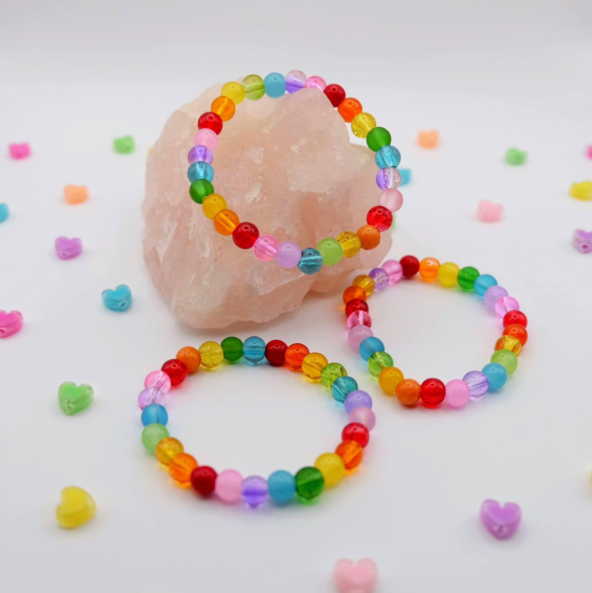 Colorful beaded bracelets on a white background with small heart-shaped beads scattered around.