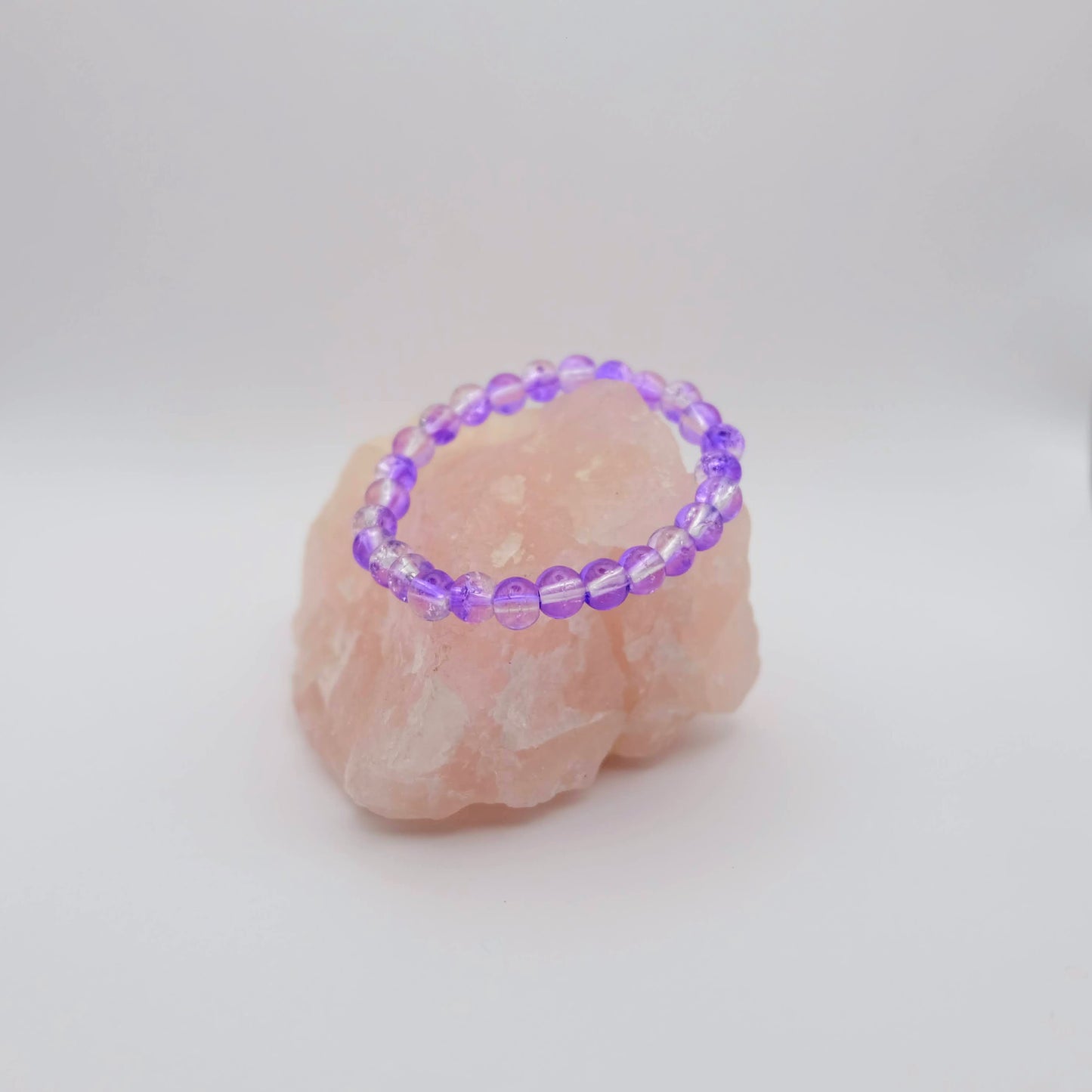Purple beaded bracelet on a pink stone with a white background