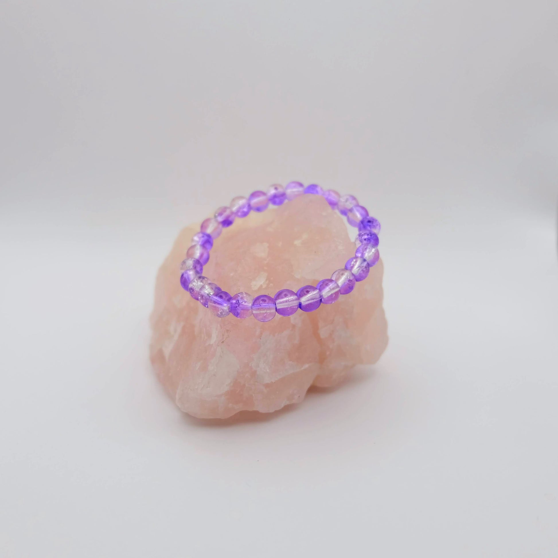 Purple beaded bracelet on a pink stone with a white background