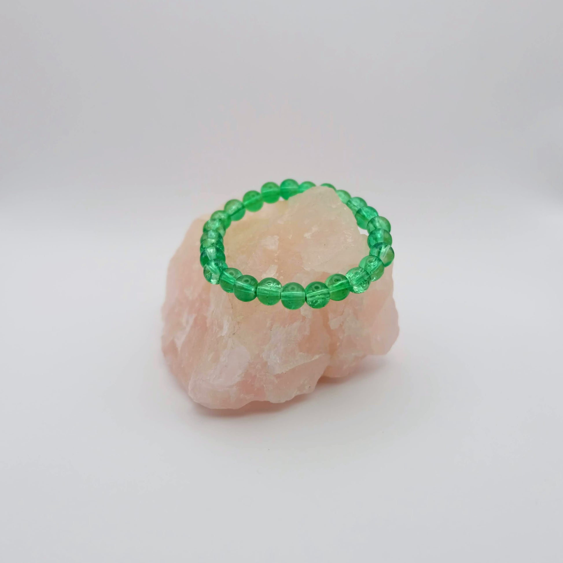 Green/Aqua beaded bracelet on a pink stone with a white background