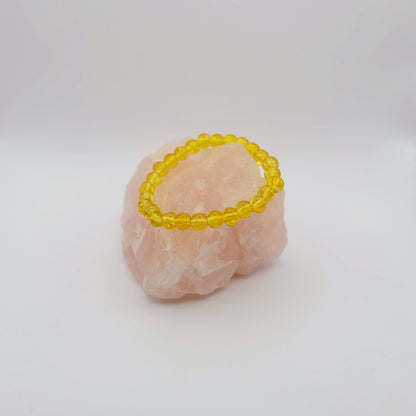 Yellow beaded bracelet on a pink stone with a white background